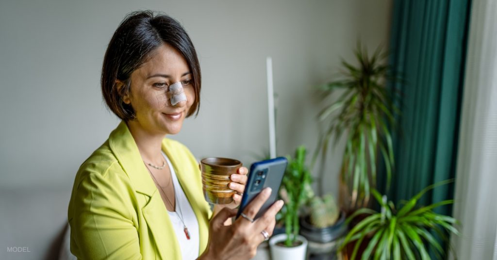 middle-aged woman with bandages on her nose for recovery looking at her phone (model)